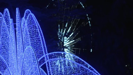 Ferris wheel rotates slowly behind a neon light sculpture