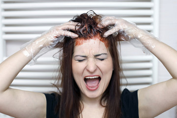 Woman in process of hair coloring at home. Applying red color to the hair and screaming.