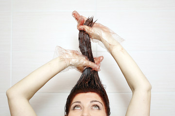 Woman in process of hair coloring at home. Applying red color to the hair and looking up.