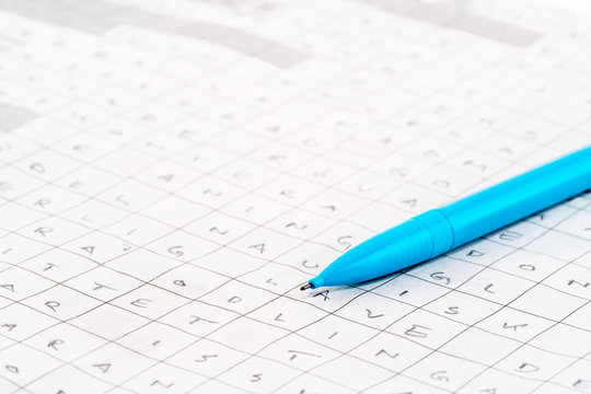Leisure activity. Close-up of a blue pen on a newspaper crossword puzzle with letters.