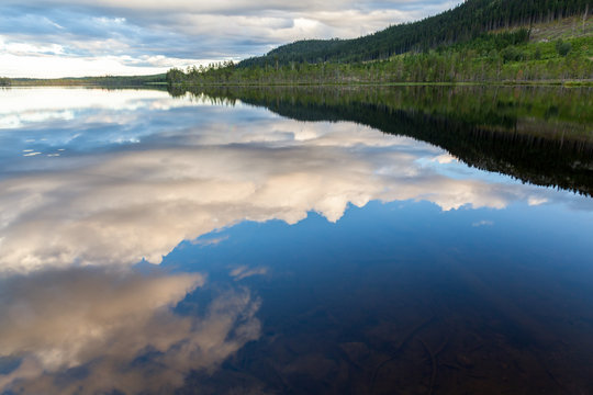 Beautiful landscape view of mountains, forest and cloudy sky reflection in calm water.