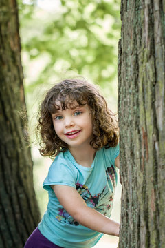 Close up summer portrait of a cute pretty smiling preschool girl with tangled hair, standing between two trees.