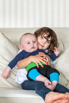 Cute portrait of sister and brother siblings holding each other on a couch. Small girl and a baby boy.