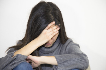 Closeup portrait of a stressed woman in a deep pain. Her face is pressed against her hands. Alone and lonely young girl feeling depressed. 
