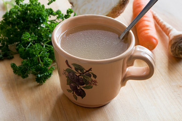 Chicken bone broth in a mug with vegetables in the background