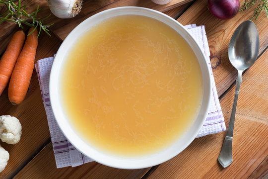 Bone broth made from chicken on a wooden table, top view
