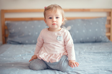 Portrait of cute adorable Caucasian blonde smiling baby girl with blue eyes in pink shirt sitting...