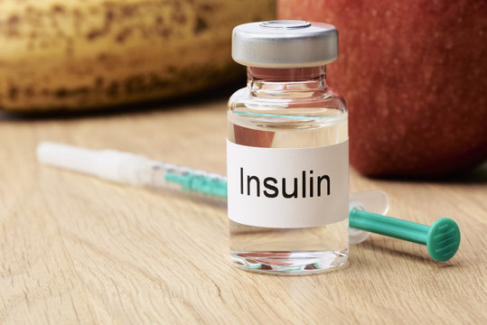 Diabetes - Eine Ampulle mit Insulin steht auf einem Tisch und daneben liegt eine Spritze. Im Hintergrund sind eine Apfel und eine Banane zu sehen