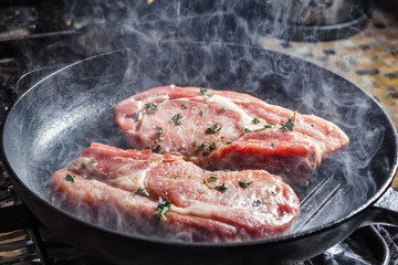 Smoke rises above natural pork cutlets with seasoned pepper, salt, garlic and thyme, frying in a grill pan
