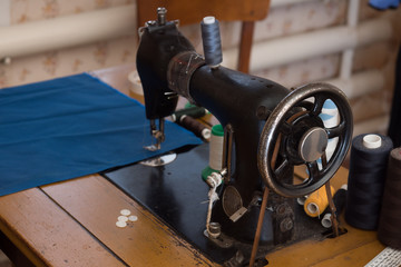 The old sewing machine is sewn blue cloth in the home workshop