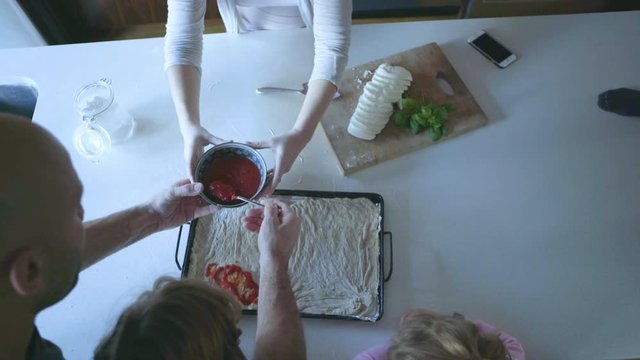 High angle dolly shot of family preparing pizza in kitchen at home