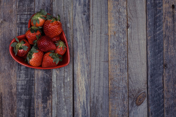 Heart shaped bowl of strawberries on wooden background