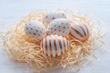 Golden Easter eggs in straw nest on white wooden rustic vintage background.