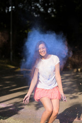 Happy brunette asian woman jumping with Holi paint exploding around her