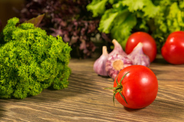 Juicy tomato and garlic on a wooden table. Green salad in the background.