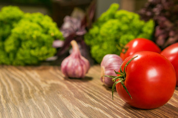Ripe tomatoes and garlic on a wooden table with fresh herbs in the background. Food Ingredients