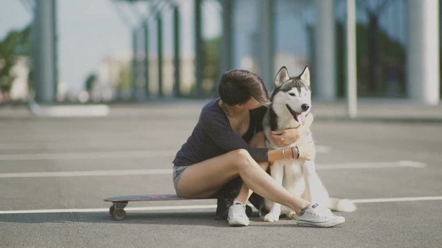 Young beautiful woman on the street hugging her husky dog sitting on a skateboard or longboard 
