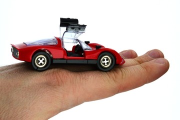 Red plastic model of street-legal german racing car standing on back of adult male hand, opened gullwing doors, white background