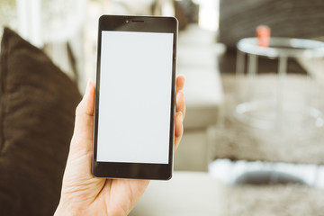 Women hand holding mobile smart phone with blank screen  in a modern style living room to checking e-mail or social network. Technology and lifestyle concept.