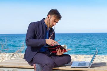 Young man using mobile devices phone and laptop outdoors. 