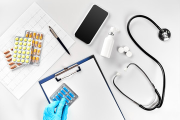 Workplace of a doctor. Pills in hand, stethoscope, clipboard and glasses on white table