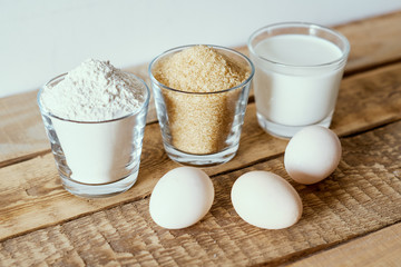fresh milk, flour, eggs and sugar on a wooden table prepared for baking a cake