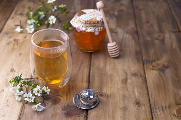 A glass with tea, spring white flowers. Bank with honey. Wooden background and free space for text or cards.