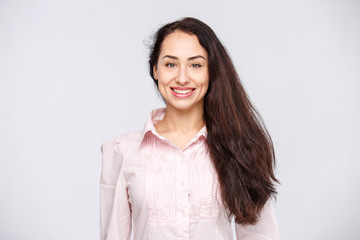 Fototapeta premium Portrait of a young woman with a charming toothy smile, black hair and brown eyes on a white background in a pink shirt. Positive and joyful emotions