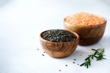 Assorted lentils. Marble, red and black raw organic lentils in wooden bowls with rosemary on grey concrete background. Copy space