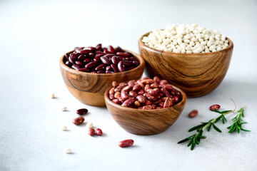 Various of kidney beans. Red, white and black kidney beans in wooden bowls with rosemary on grey concrete background. Copy space, banner