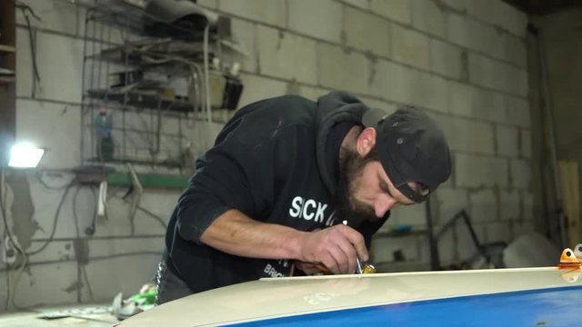 Adult bearded man mechanic concentrates painting with airbrush on the car hood