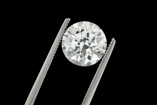 Diamond : loose brilliant 4 carats diamond is being held by a tweezers on black background