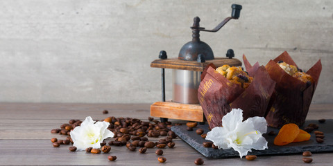 Coffee grinder, two muffins, aroma coffee grains and flowers of azalia on black stone.