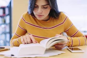 Young woman reading a book while sitting in library