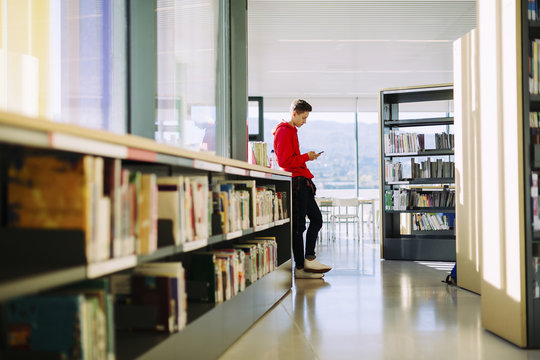 Side view of man using mobile phone while standing in library