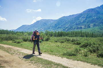 Young woman hiker with backpack and trekking poles on a sunny day on mountain trail