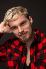 Handsome trendy young guy at the studio on black background. He wears beard and a plaid shirt