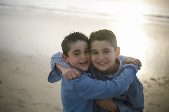 Portrait of happy brothers standing at beach during sunset