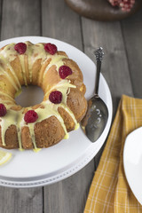 Lemon cake frosted with yellow sugar icing and red raspberries, dressed with lemon slices on the side on a white platter