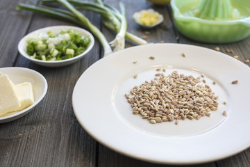 Plate of uncooked farro grains with onions, lemons, butter and rind as ingredients for a recipe