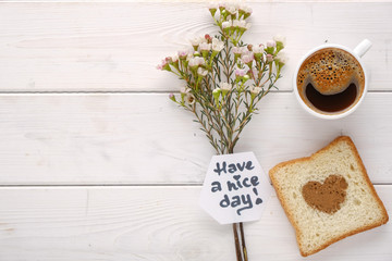 Coffee cup with flowers and toast with heart shaped cinnamon top view on white wood background
