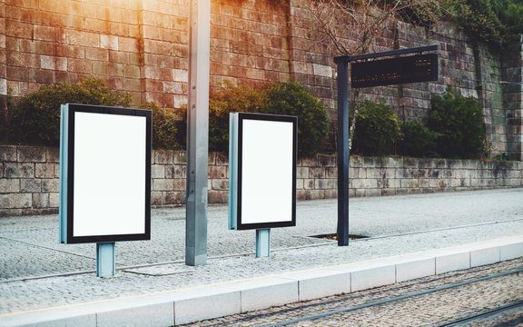 Template of two empty city billboards on train station outdoors or metro station; mock-up of blank informational banners in urban settings near tram stop with electronic indicator panel behind