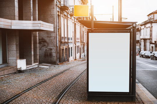 Close-up view of empty white informational banner mockup in urban settings between road and tramway; blank billboard placeholder template outdoors on city tram stop, pavement stone, sunny day