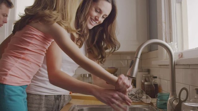Handheld shot of mother washing daughter's hand at kitchen sink