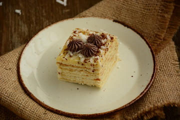 Piece of cake napoleon on a plate with chocolate candys,  custard and coconut chips  