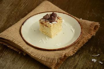 Piece of cake napoleon on a plate with chocolate candys,  custard and coconut chips  