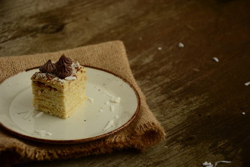Piece of cake napoleon on a plate with chocolate candys,  custard and coconut chips  