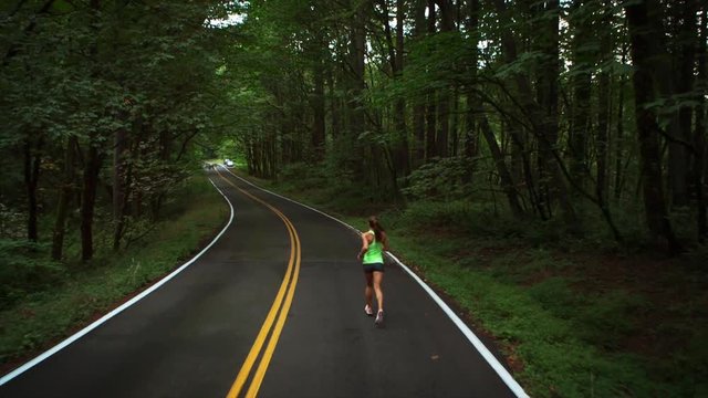 Handheld shot of female athlete jogging on road in forest