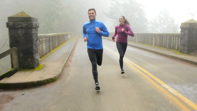 Handheld shot of happy couple jogging on elevated road during foggy weather