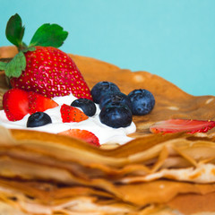 Side view of stack of thin pancakes poured with sour cream and decorated with fresh strawberries and blueberries. The concept of Russian holiday Maslenitsa, Shrovetide